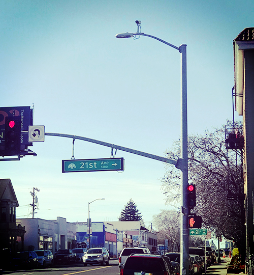 Street sign says 21st Ave. There's a CCTV camera above.